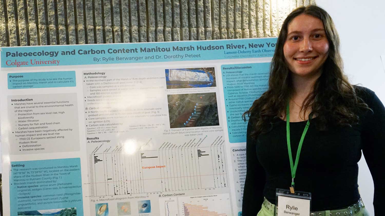 Person smiling and standing next to a project presentation poster.